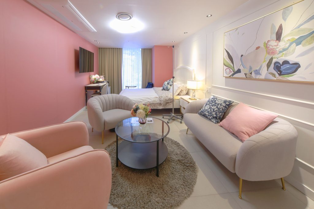 Recovery suite with a bed, rose-coloured wall, lounge chairs and a round table